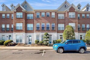 Une rangée de maisons de ville avec un parking et un SUV bleu garé devant.