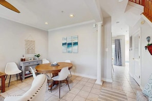 A dining area with a round table, white chairs, and a wall-mounted macrame piece. - The Villages of Five Points condo w/community pools, tennis courts, shops (Lewes)
