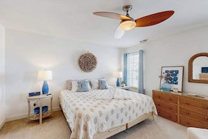A bedroom with a bed, a ceiling fan, a bedside table, a dresser, a mirror, and a wall decoration. - The Villages of Five Points condo w/community pools, tennis courts, shops (Lewes)