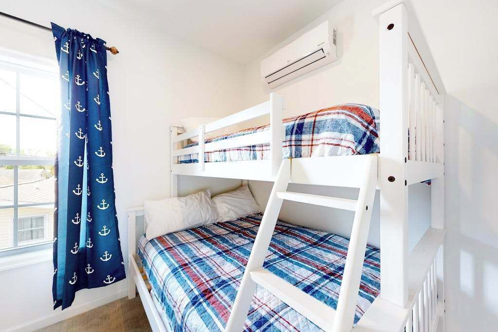 A bunk bed room with a window, curtains, and an air conditioning unit.