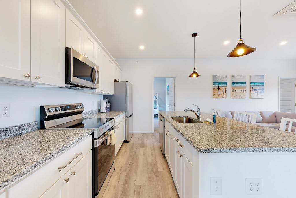 A modern kitchen with white cabinetry, granite countertops, stainless steel appliances, and pendant lighting.