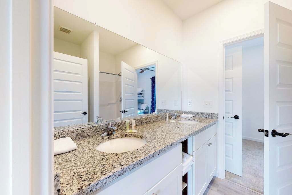 Un baño con lavamanos blanco, encimera de granito y un espejo grande.