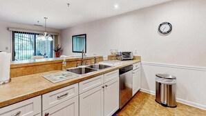 Una cocina moderna con armarios blancos, electrodomésticos de acero inoxidable y un ventanal con persianas.