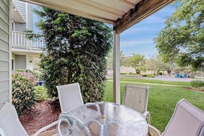 A covered patio with a glass table and chairs, surrounded by greenery and a view of a residential street. - Spring Lake dog-friendly gem with private patio, fireplace, W/D, shared pool, (Rehoboth Beach)
