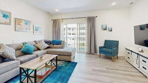 A modern living room with a sofa, armchair, coffee table, and a TV. - Bayfront Condo | View, Near Lewes Beaches (Lewes)
