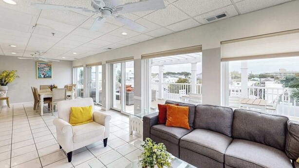 A spacious living area with a ceiling fan, large windows, a sofa, a chair, and a dining table. - Town of Rehoboth Beach apartment w/balcony, walk to beach (Rehoboth Beach)
