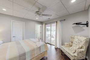 Une chambre à coucher comprenant un lit, une chaise, un ventilateur de plafond et une porte-fenêtre coulissante.