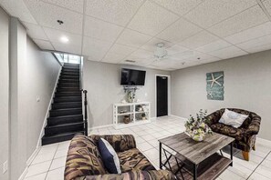 Un salon avec un escalier, un téléviseur à écran plat, une console blanche, un canapé à motifs, une table basse en bois et un élément décoratif mural.