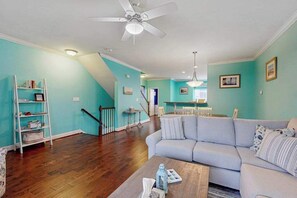 A living room with a sofa, a coffee table, a bookshelf, and a staircase. - Rehoboth Crossing Townhouse: Pool, AC and minutes from downtown Rehoboth Beach (Rehoboth Beach)