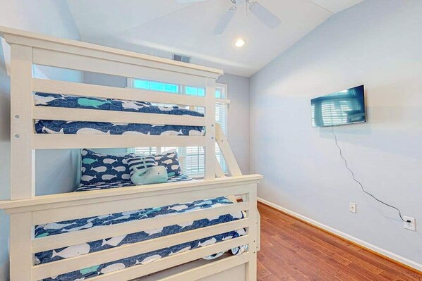 A bunk bed with a TV mounted on the wall, wooden flooring, and a ceiling fan. - The Tides - Relaxing stay with a patio and grill - pool & easy beach access (Rehoboth Beach)