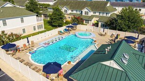 Ein Schwimmbecken mit Liegestühlen und Sonnenschirmen, umgeben von wohngebäudelichen Bauten mit begrünten Dächern.