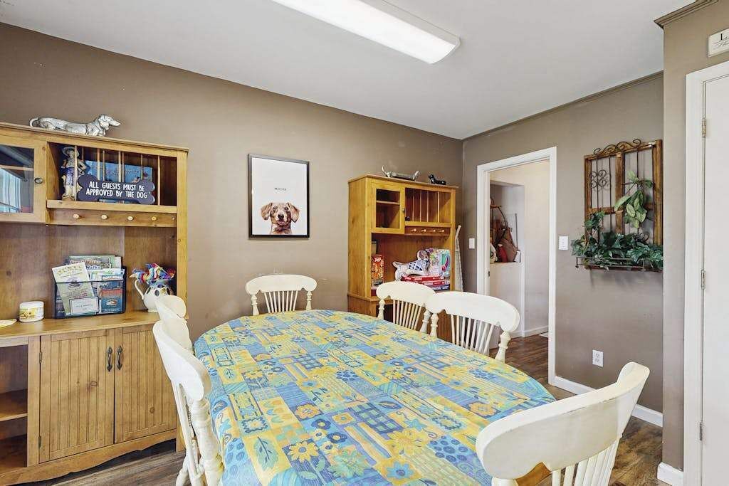 A dining area with a table, chairs, wooden cabinets, and a framed picture on the wall.