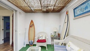 Una stanza con un divano in vimini, una sedia con un cuscino rosso, un'asse da surf e un tavolino in vetro.