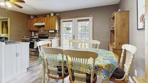 Una cucina con mobili bianchi, un tavolo da pranzo con sedie, una ventola a soffitto e una finestra con vista.