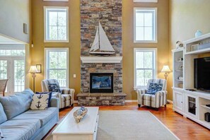 A living room with a stone fireplace, a sailboat decoration, and a television. - Coastal home near the beach with pool, tennis, game room, WiFi, AC (Rehoboth Beach)