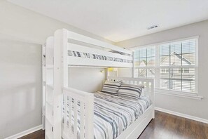 A bunk bed with a striped bedspread, a window with blinds, and a view of a house outside. - Eagles Landing townhome with pool and tennis access, patio & grill (Rehoboth Beach)