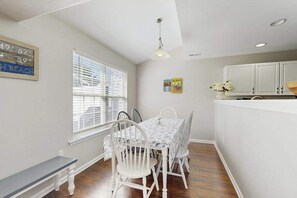 A dining area with a table and chairs, a bench, a window with blinds, and a kitchen area with cabinets. - Eagles Landing townhome with pool and tennis access, patio & grill (Rehoboth Beach)