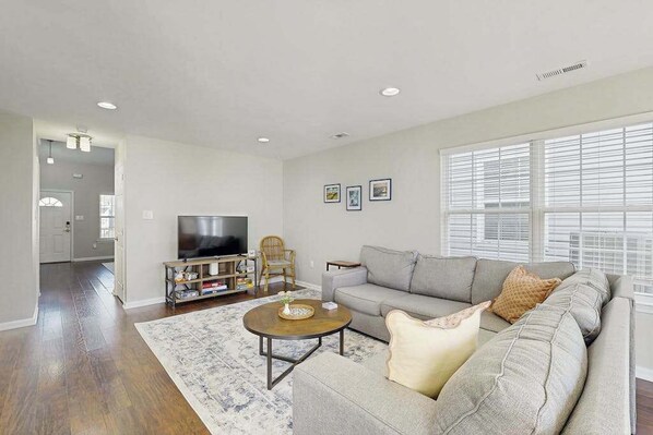 A living room with a sofa, coffee table, TV, and bookshelf. - Eagles Landing townhome with pool and tennis access, patio & grill (Rehoboth Beach)