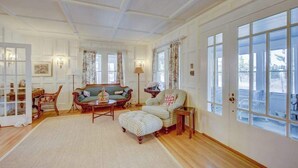Un salon spacieux comprenant un canapé, un fauteuil, un pouf et une grande fenêtre avec des rideaux.