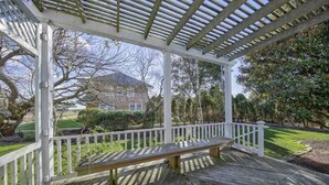 Une véranda avec un banc, des balustrades blanches et une vue sur une maison et un jardin.