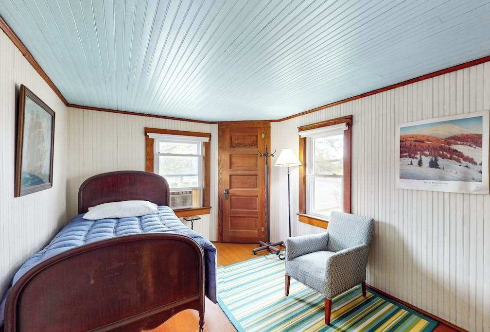 A bedroom with a bed, a chair, a door, and a window.