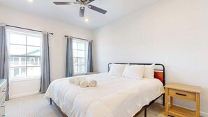 Een slaapkamer met een bed, nachtkastje, plafondventilator en een raam met gordijnen.
