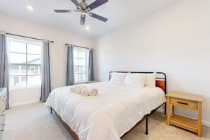 A bedroom with a bed, a bedside table, a ceiling fan, and a window with curtains. - Rehoboth Beach House condo with all-new interior, on-site pool, & washer/dryer (Rehoboth Beach)