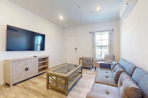 A living room with a sofa, a coffee table, a TV, and a cabinet. - Rehoboth Beach House condo with all-new interior, on-site pool, & washer/dryer (Rehoboth Beach)