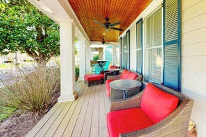 A covered porch with wicker furniture and red cushions, wooden ceiling, and large windows with shutters. - Elegant house near the ocean with AC, W/D & outdoor space - walk to boardwalk (Rehoboth Beach)