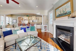 A spacious living room with a fireplace, a sofa set, and a kitchen in the background. - Elegant house near the ocean with AC, W/D & outdoor space - walk to boardwalk (Rehoboth Beach)