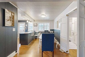 A modern kitchen with a central island, a dining area with a blue chair, and a hallway leading to a door. - Spacious dog-friendly house with enclosed porch and yard- perfect for families! (Rehoboth Beach)