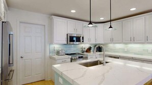 Una cocina moderna con armarios blancos, electrodomésticos de acero inoxidable, encimera de mármol e iluminación colgante.