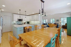 A spacious kitchen with white cabinets, a wooden dining table, and a seating area with a sofa and chairs. - Saltbox home near the ocean with WiFi, central AC, enclosed yard, washer/dryer (Rehoboth Beach)
