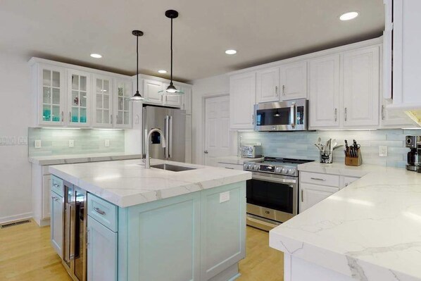 A modern kitchen with white cabinets, stainless steel appliances, and a marble countertop. - Saltbox home near the ocean with WiFi, central AC, enclosed yard, washer/dryer (Rehoboth Beach)