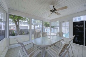 Eine überdachte Terrasse mit Tisch und Stühlen, einem Deckenventilator und einem 'Willkommen' Schild.