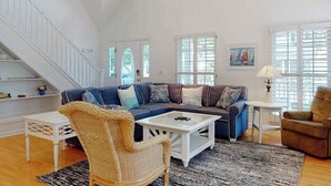 Un salón amplio con un sofá grande, un sillón de mimbre, una mesa de centro y una escalera.