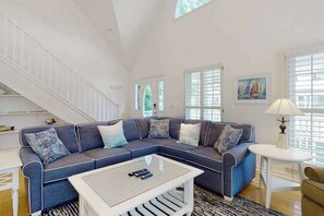 A living room with a sectional sofa, a coffee table, a lamp, and a staircase. - Saltbox home near the ocean with WiFi, central AC, enclosed yard, washer/dryer (Rehoboth Beach)