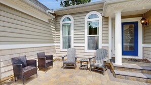 Un patio cubierto con mobiliario exterior, una puerta azul y una ventana con un diseño decorativo en el vidrio.