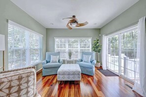 A spacious room with two sofas, a ceiling fan, large windows, and a wooden floor. - Coastal Luxury & Community Charm: Your Rehoboth Beach Retreat (Rehoboth Beach)