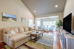 A living room with a sofa, coffee table, television, and a view into another room. - Coastal Luxury & Community Charm: Your Rehoboth Beach Retreat (Rehoboth Beach)