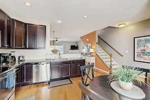 A modern kitchen with dark cabinetry, stainless steel appliances, and a dining area with a table and chairs. - Rehoboth Crossing townhome - pool & gym - dog-friendly, fireplace & private W/D (Rehoboth Beach)