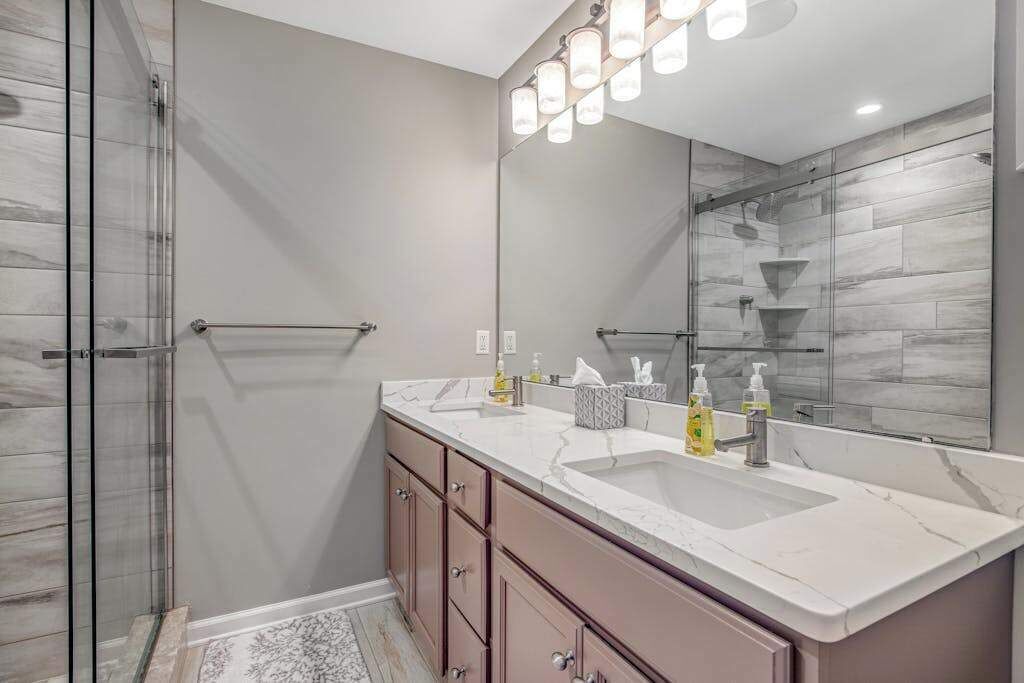 Une salle de bain moderne avec une douche à l’italienne en verre, un grand miroir et un plan de toilette en marbre.