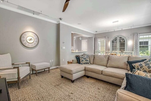 A living room with a sectional sofa, a small table, and a clock on the wall. - Oyster Bay Villas with pool, central AC, fast WiFi, & washer/dryer. Dogs ok (Rehoboth Beach)