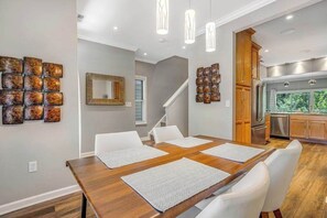 A dining area with a wooden table, white chairs, and artwork on the walls. - Oyster Bay Villas with pool, central AC, fast WiFi, & washer/dryer. Dogs ok (Rehoboth Beach)