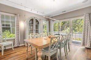 A dining room with a wooden table and chairs, large windows with curtains, and a view of greenery outside. - Oyster Bay Villas with pool, central AC, fast WiFi, & washer/dryer. Dogs ok (Rehoboth Beach)
