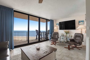 A room with a large sliding glass door to the beach, a flat-screen TV, two leather chairs, a wooden coffee table, and a small side table with a lamp. - Sea Colony 8th floor condo w/ free WiFi, balcony, shared pool & ocean view (Bethany Beach)