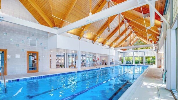 Ein Hallenbad mit Holzbalkendecke, deutlich abgetrennten Bahnen und angrenzenden Geschäften.