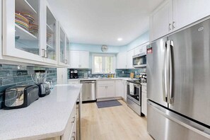 Una cocina moderna con electrodomésticos de acero inoxidable, armarios blancos y un salpicadero azul.