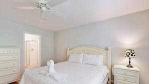 Ein Schlafzimmer mit Bett, Nachttisch, Lampe, Kommode und Deckenventilator.