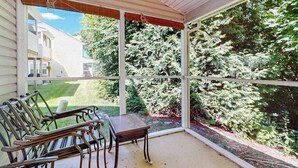 Eine überdachte Veranda mit Tisch und Stühlen, großen Fenstern und Blick auf ein Haus und Bäume.